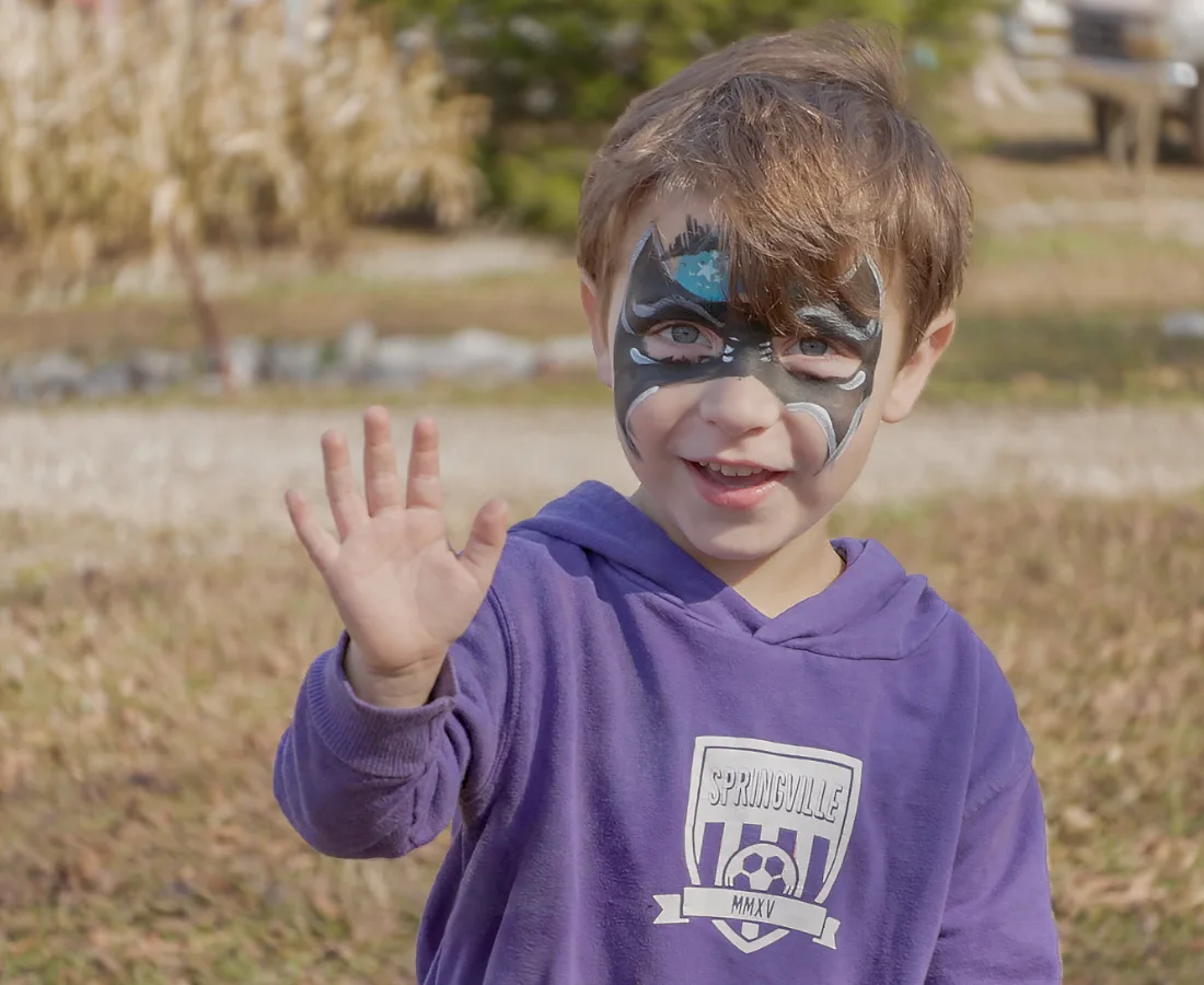A child with face paint waving at the festival