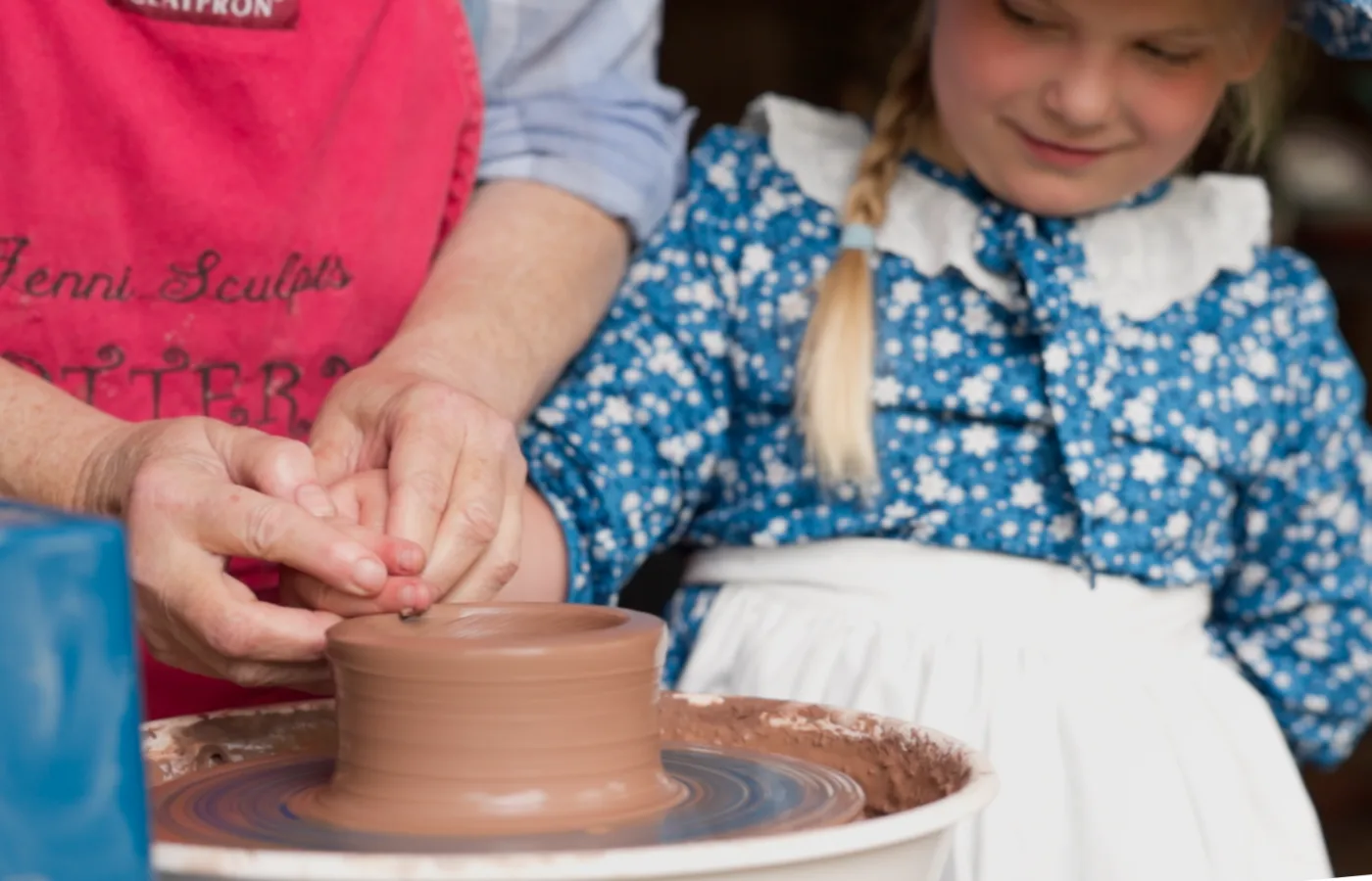 A potter guiding a child's hands on the wheel at a craft demonstration